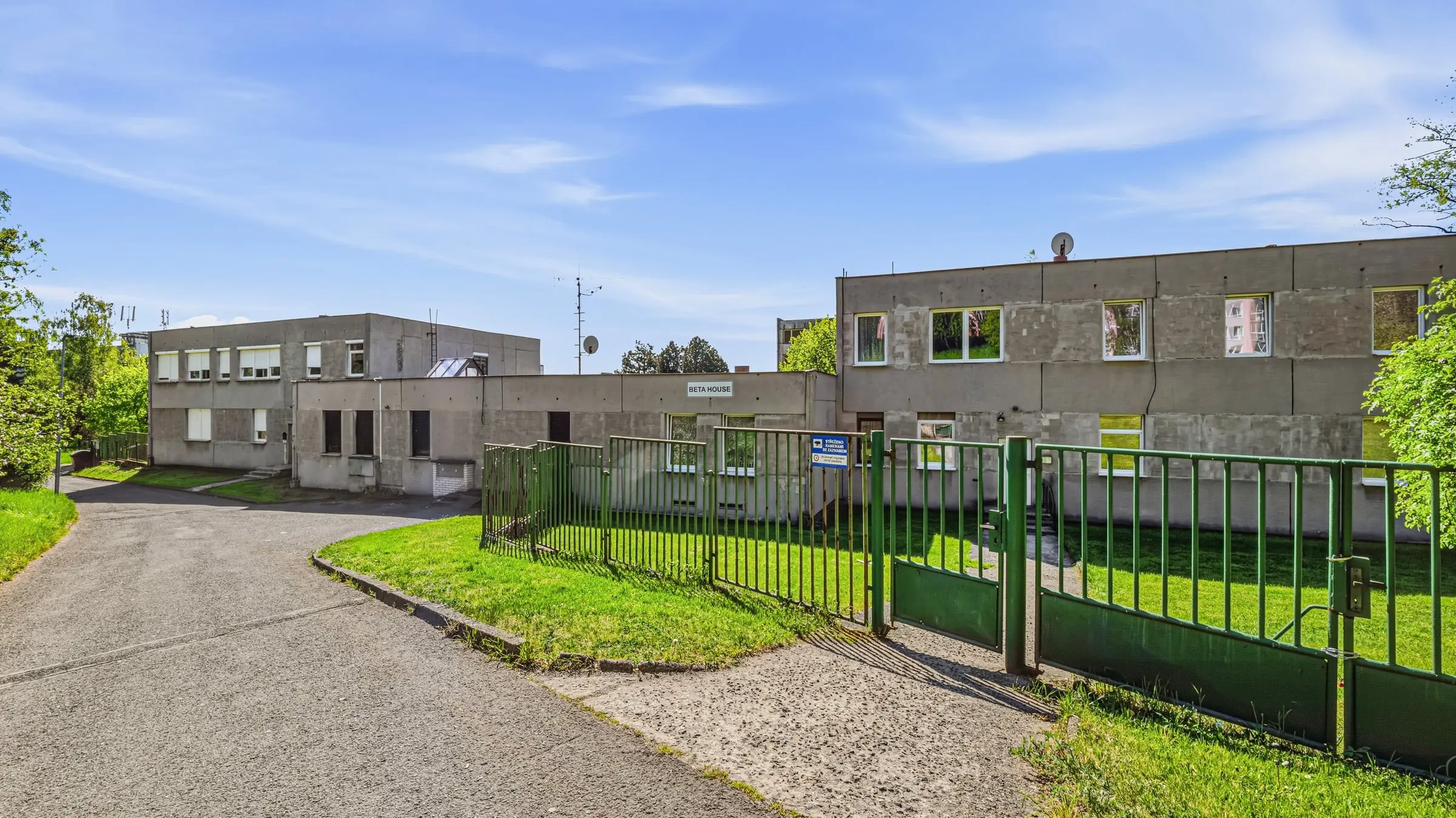 Zelená brána a oplocení u vjezdu do areálu, na budově nápis Beta House